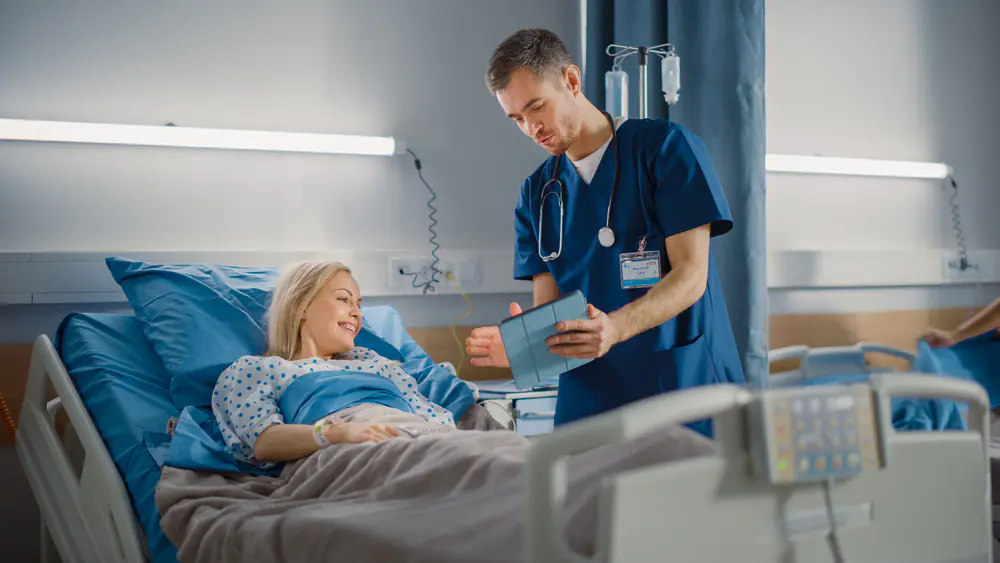 Male nurse smiling and talking with a female patient in a hospital bed