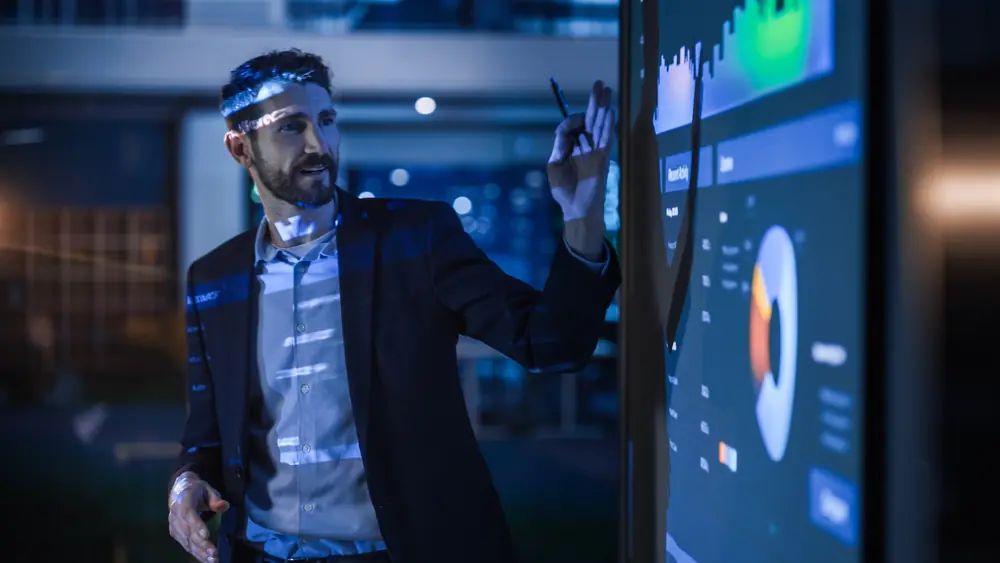 A male in a suit stands in front of a board presenting data findings