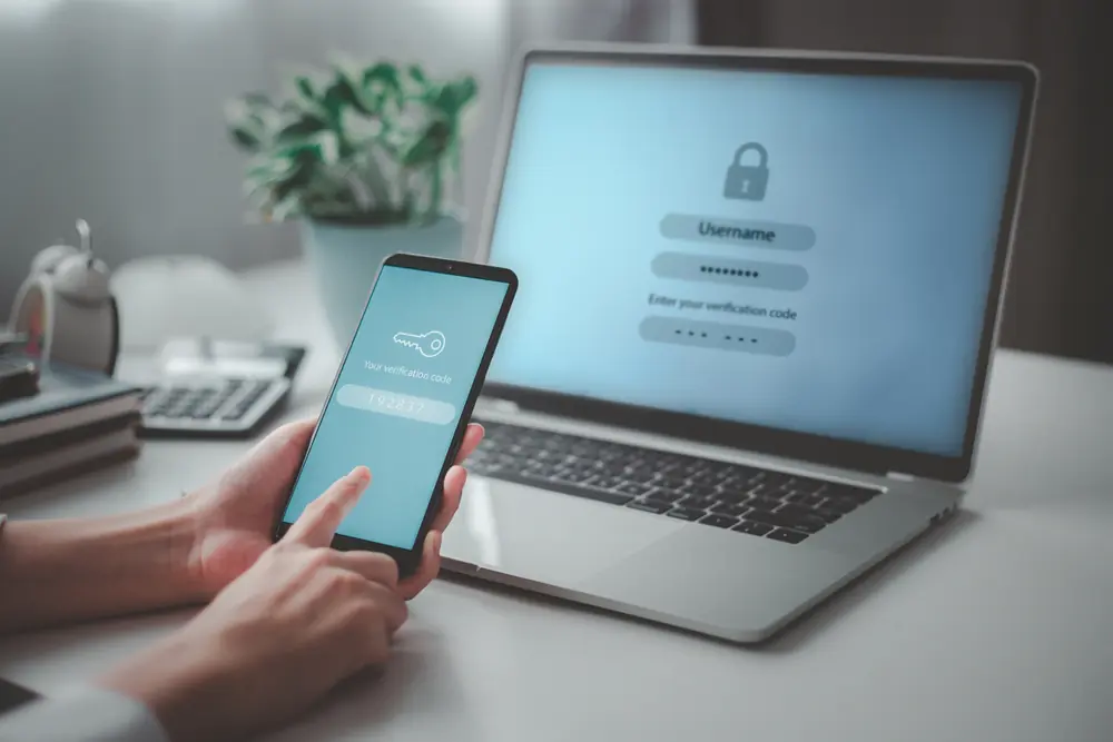 Person holding a phone in front of their laptop where both devices have a authentication screen