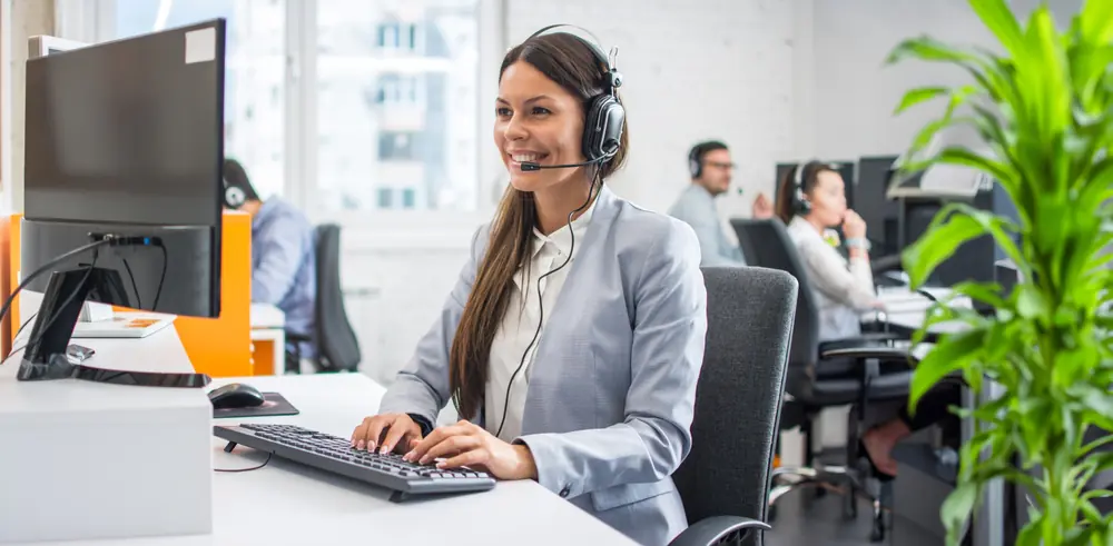 Smiling woman in front of monitor providing phone support in an office setting