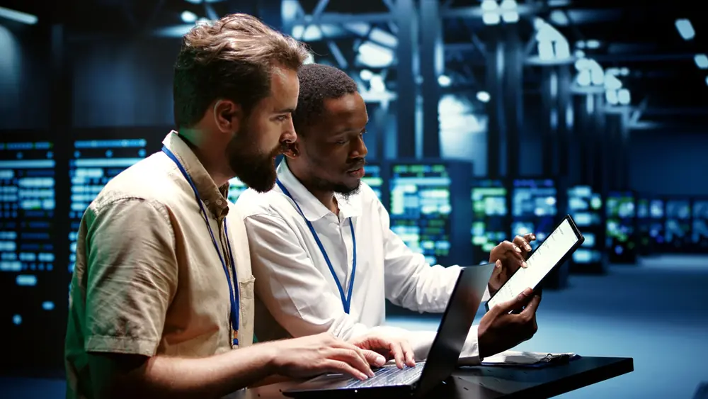 Two males looking at a device with modern data centre racks in the background