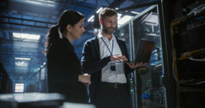 Male and female IT technicians in front of a laptop in a data centre